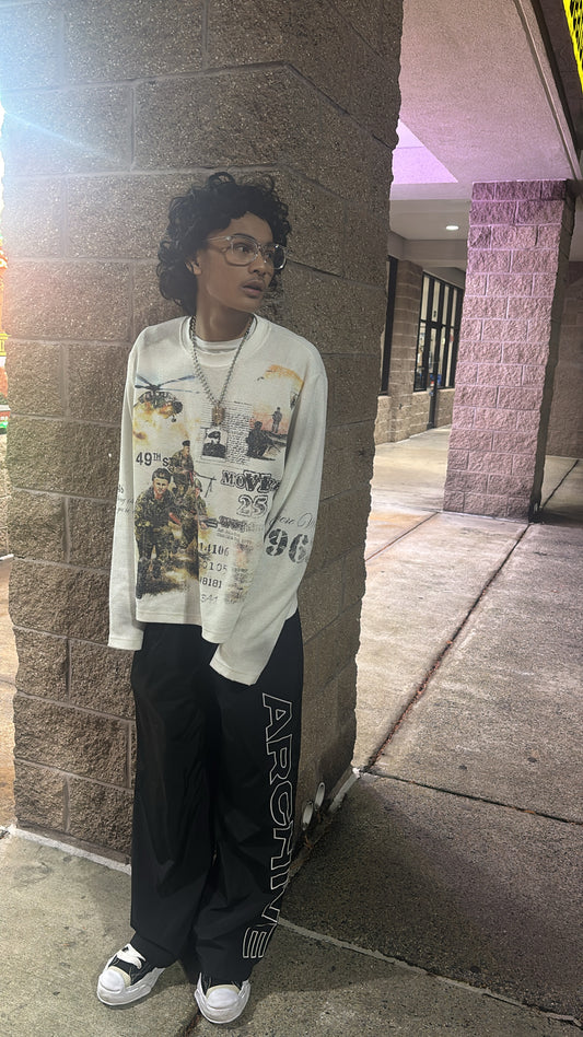 Person wearing a graphic t-shirt and dark pants leaning against a wall.